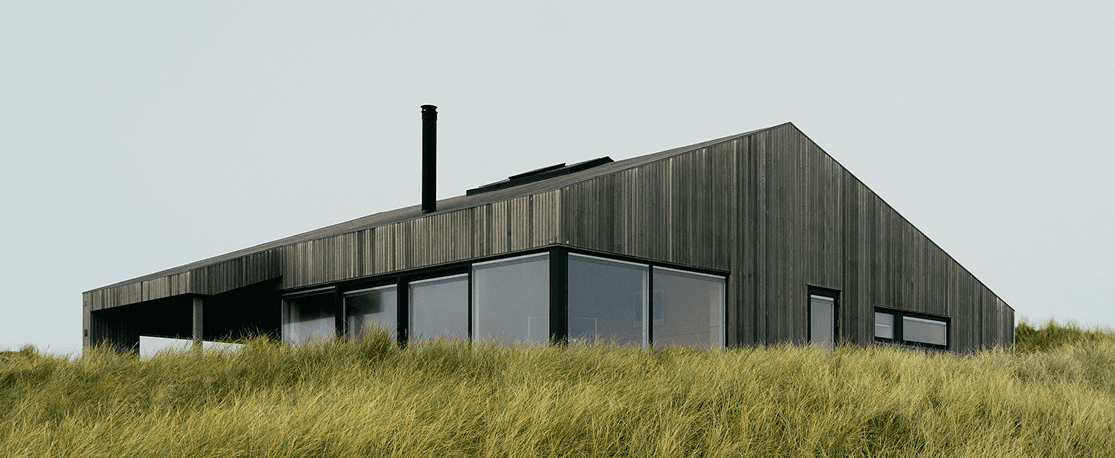 Maison en bois sombre au milieu des hautes herbes